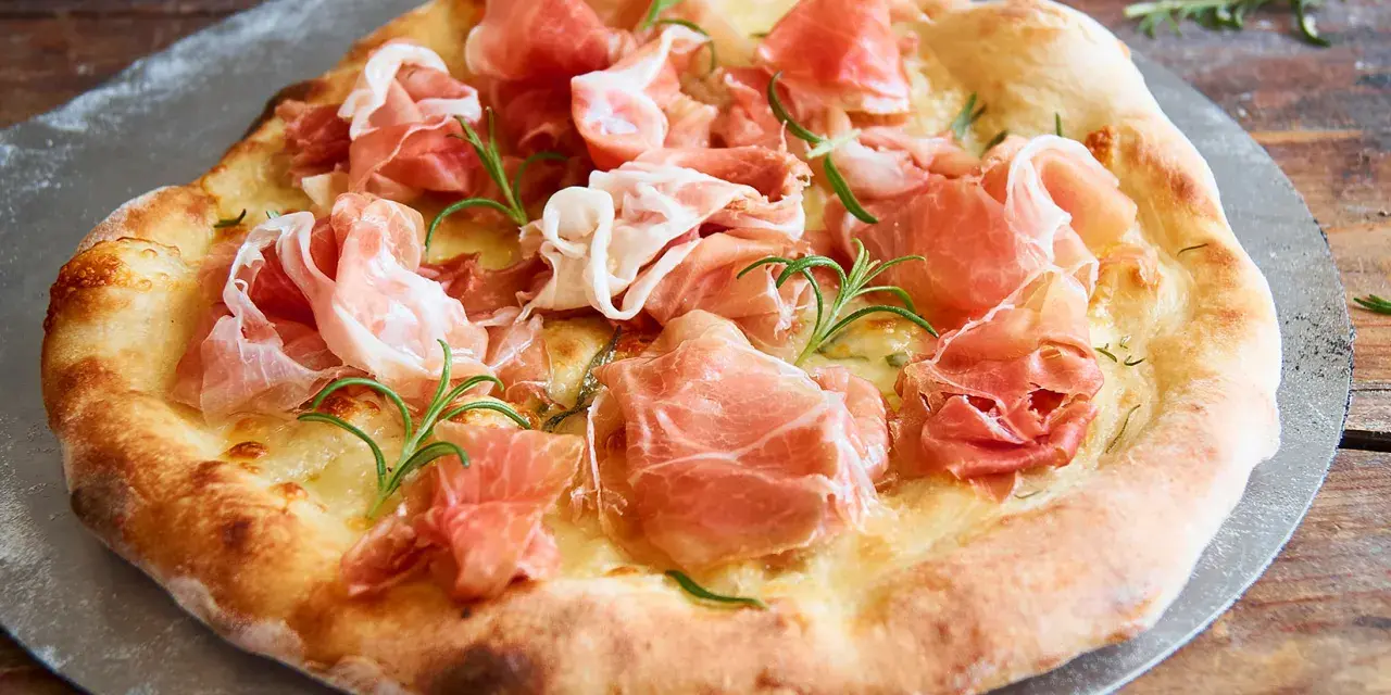 Eine köstliche biancaneve pizza mit zartem Schinken und Rosmarin, auf einem Pizzastein serviert.