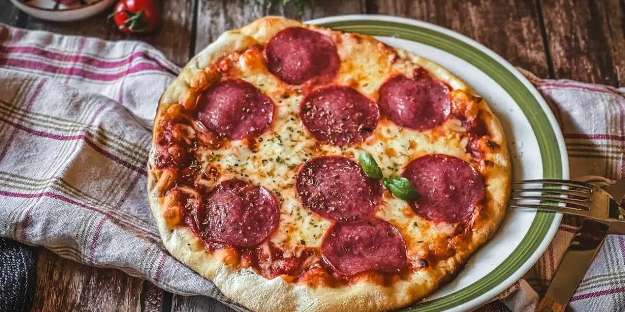Eine köstliche Pizza Salami mit geschmolzenem Käse und frischem Basilikum auf einem rustikalen Holztisch.