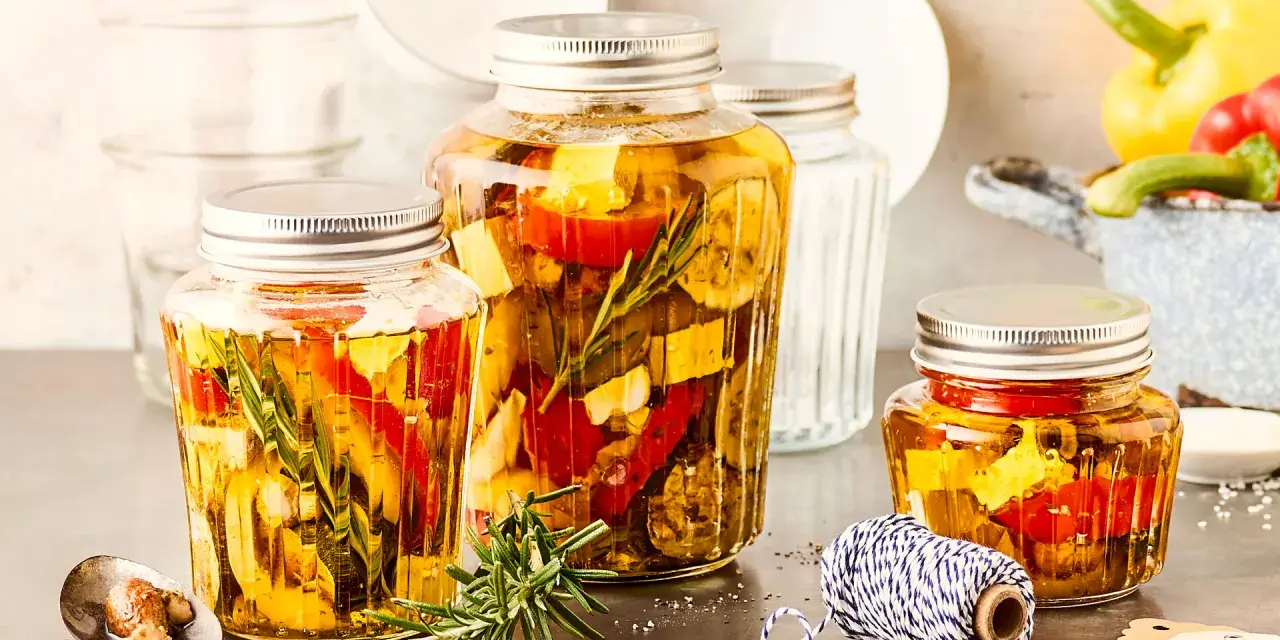Drei Gläser mit italienischem Fingerfood: eingelegtes Gemüse wie Paprika und Zucchini mit Kräutern in Öl.