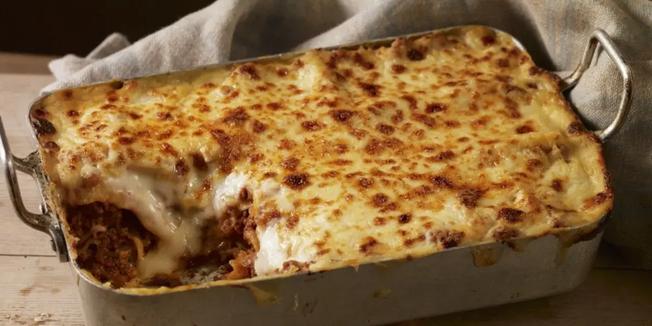 Herzhafte Lasagne mit goldbraun überbackener Käseschicht und einem Hauch von Creme Fraiche, serviert in einer Metallform auf Holztisch.