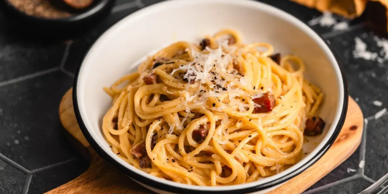 Eine Schüssel cremiger Pasta Carbonara, garniert mit frisch geriebenem Parmesan und schwarzem Pfeffer, bereit zum Genießen.