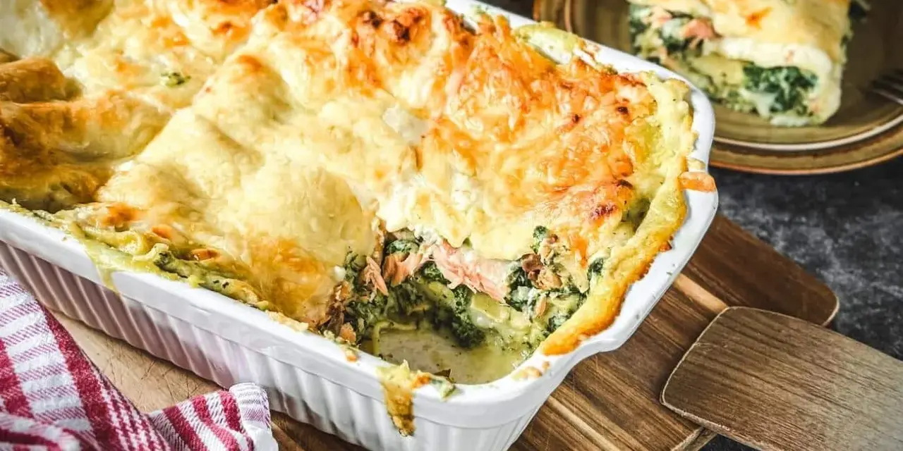 Eine köstliche, goldbraun überbackene italienische Lachslasagne mit Spinat und cremiger Sauce. Ein Stück ist bereits serviert.