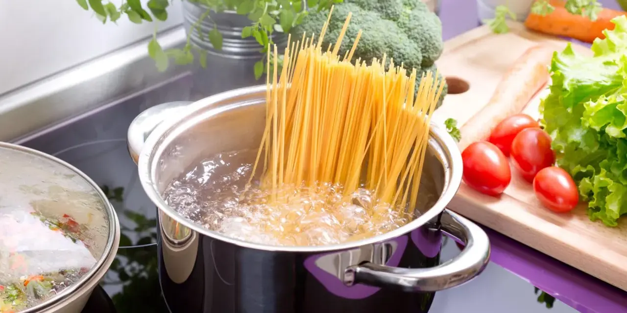 Spaghetti kochen in sprudelndem Wasser. Die richtige **Tagliatelle Kochzeit** ist entscheidend für ein perfektes Pastagericht. Frisches Gemüse wie Brokkoli, Karotten und Tomaten liegen bereit.
