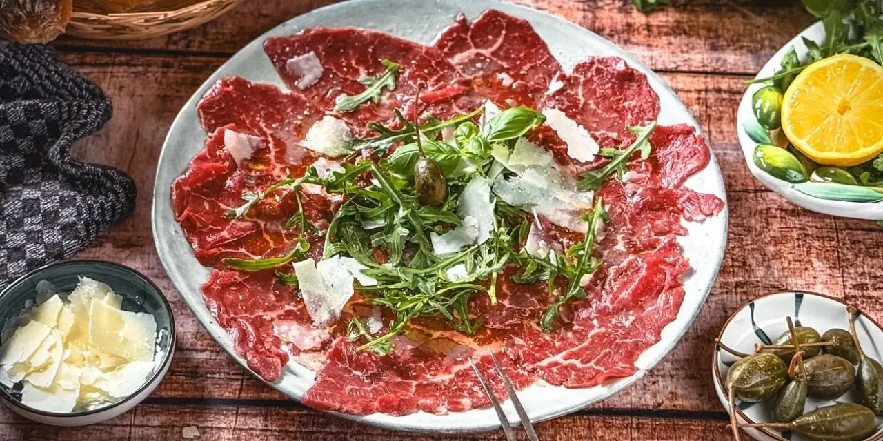 Carpaccio: hauchdünne Rindfleischscheiben mit Rucola, Parmesan und Kapern. Ein Klassiker der italienischen Küche.