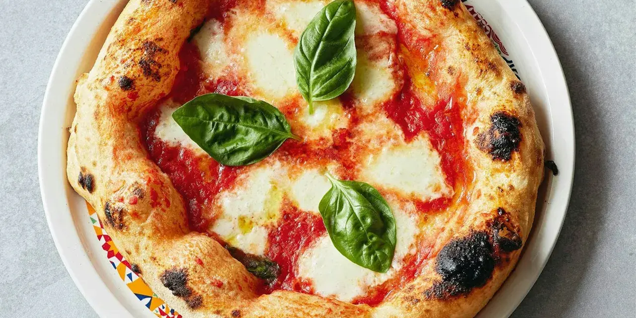Eine original Pizza Margherita mit geschmolzenem Mozzarella, Tomatensauce und frischem Basilikum. Der Rand ist goldbraun und leicht angekohlt.