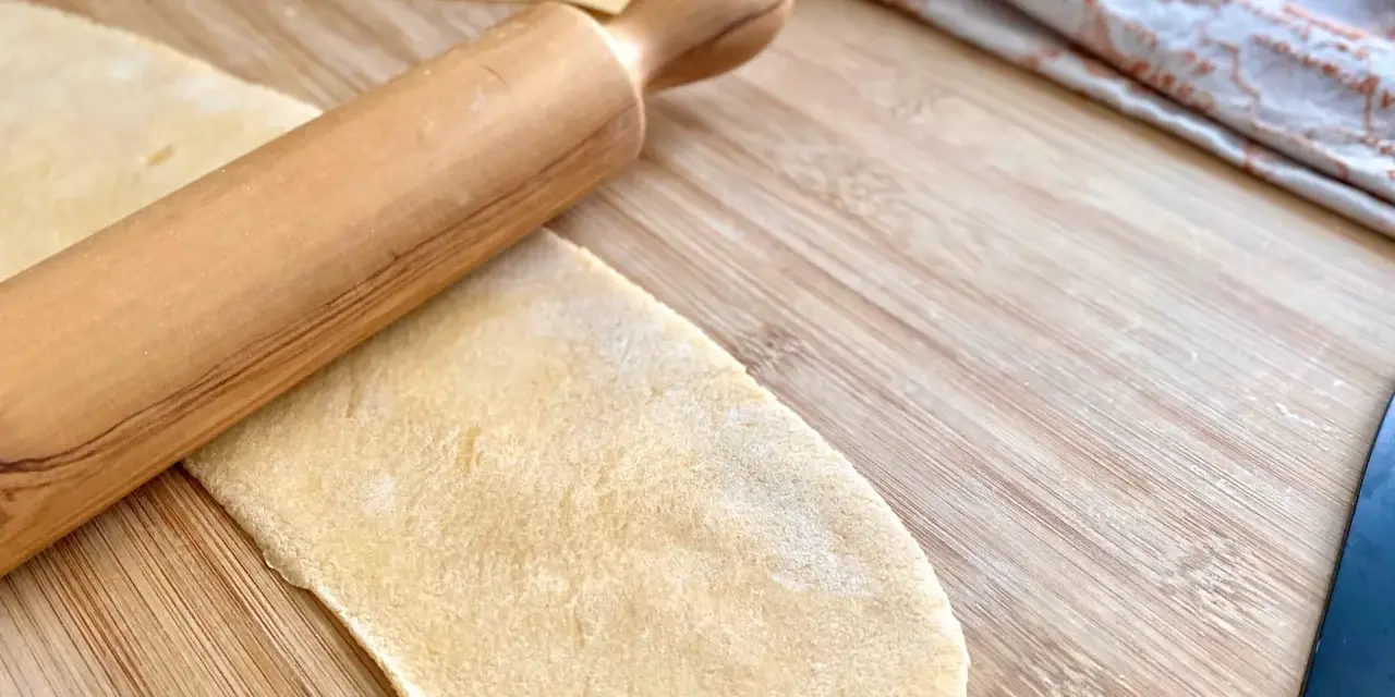 Mit einem Nudelholz wird Teig für **ravioli selber machen ohne maschine** auf einem Holzbrett ausgerollt.