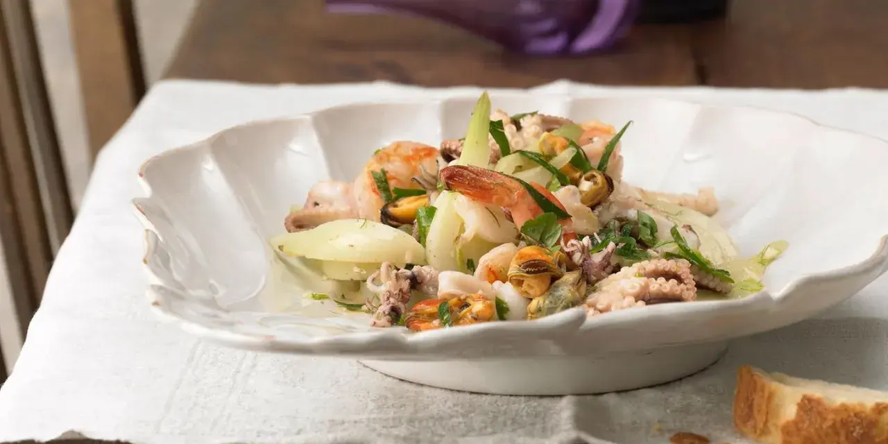 Frischer insalata di mare mit Garnelen, Muscheln und Tintenfischringen, garniert mit Kräutern und Zwiebelringen.