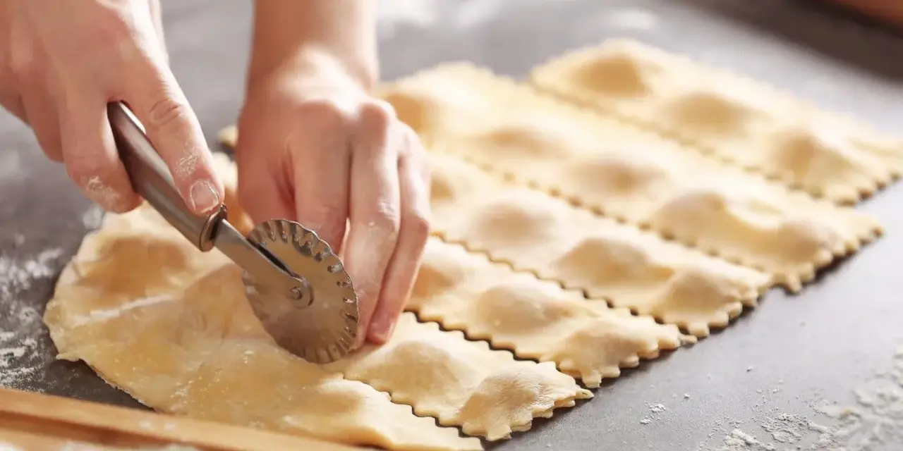 Hände schneiden mit einem Teigrädchen frische Ravioli. Das sind die besten Ravioli Rezepte zum Nachmachen.