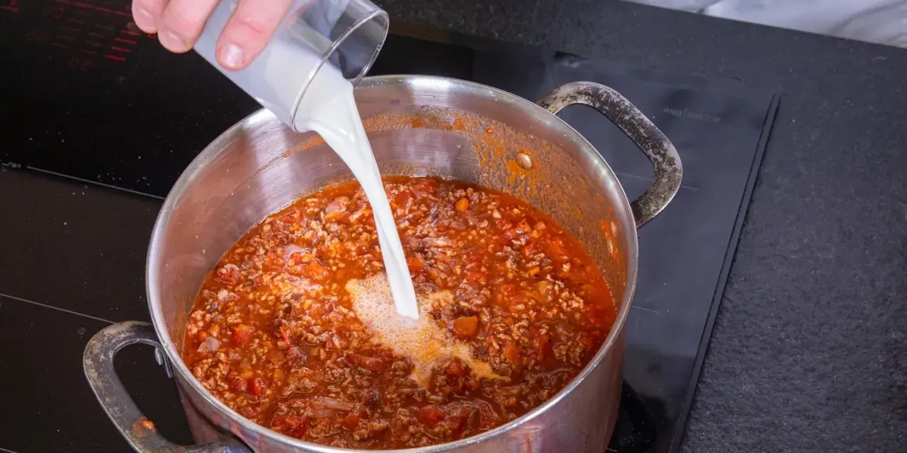 Milch wird in einen Topf mit köchelnder Bolognese gegossen, um die Sauce cremiger zu machen.