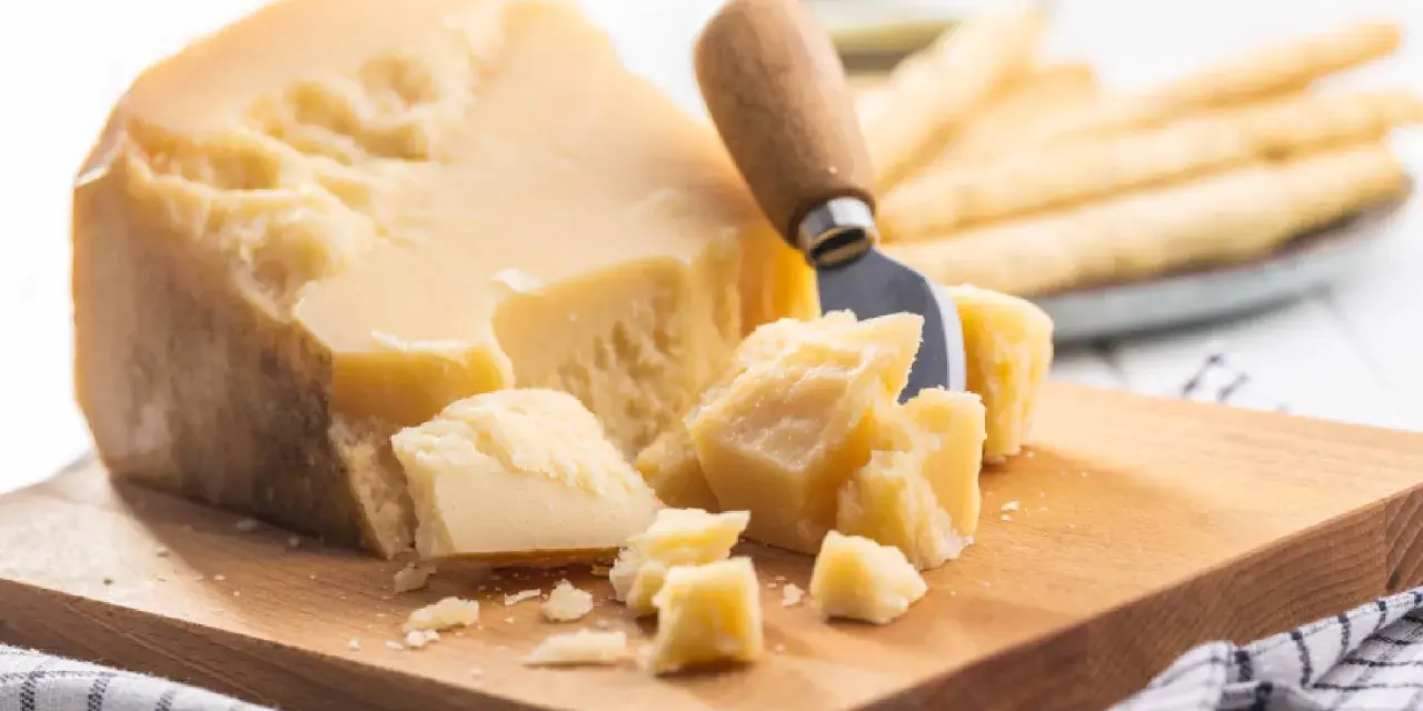 Ein Stück Parmesan mit grob abgebrochenen Stücken und einem Käsemesser. Die Parmesan Rinde ist sichtbar.