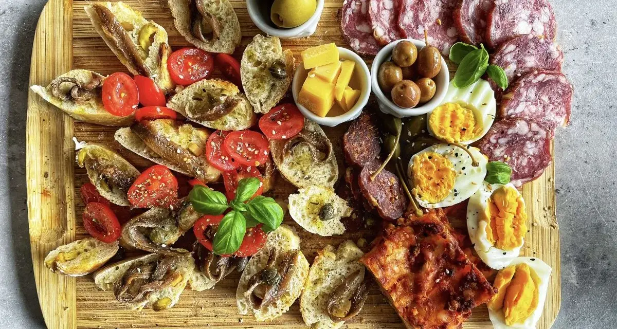 Kaltes italienisches Fingerfood: Bruschetta mit Sardellen, Tomaten, Oliven, Käse, Eiern und Salami auf Holzbrett.