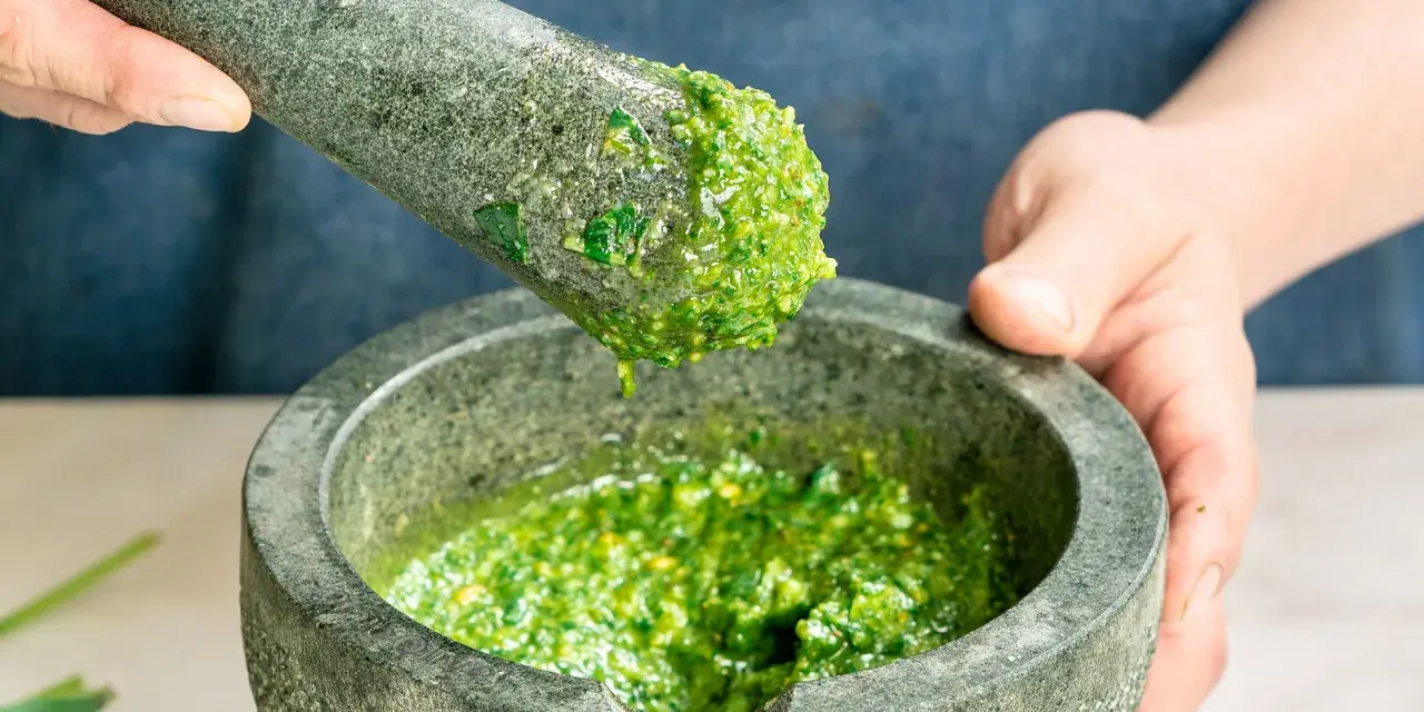 Frische Kräuter werden im Mörser zermahlen, um zu zeigen, wie man Pesto zubereitet.