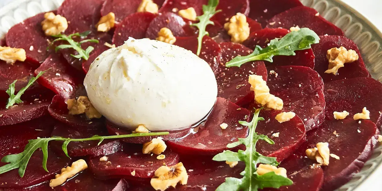 Rote Bete Carpaccio mit Burrata, Walnüssen und Rucola. Ein köstlicher Salat, der auf einem Teller serviert wird.