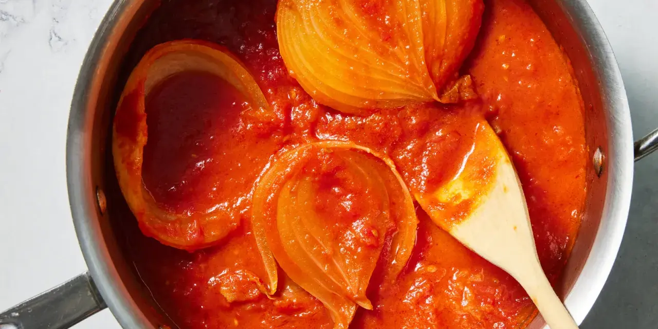 Tomatensoße mit Zwiebelstücken in einem Topf, bereit für Marcella Hazan Rezepte. Ein Holzlöffel rührt die köstliche Soße.