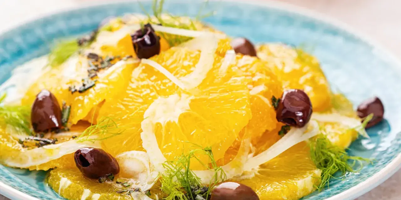 Erfrischender orangensalat sizilianisch mit Fenchel und dunklen Oliven auf einem blauen Teller.