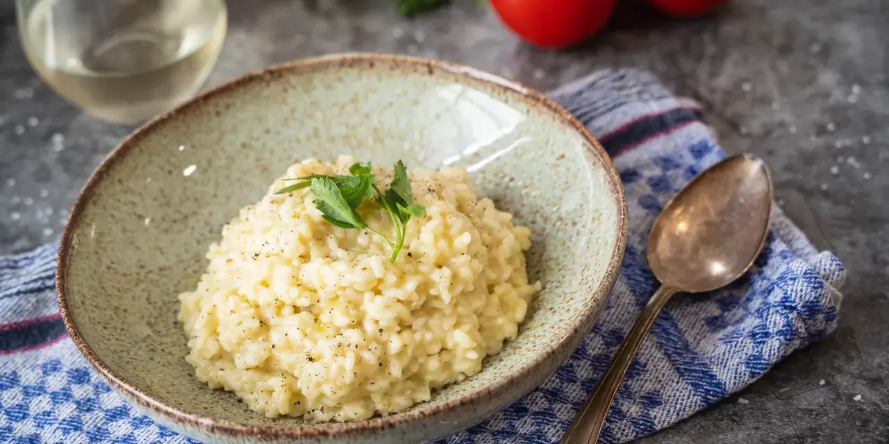 Cremiges Risotto, perfekt als Grundrezept für viele Variationen. Mit frischer Petersilie garniert, daneben ein Glas Weißwein und Tomaten.