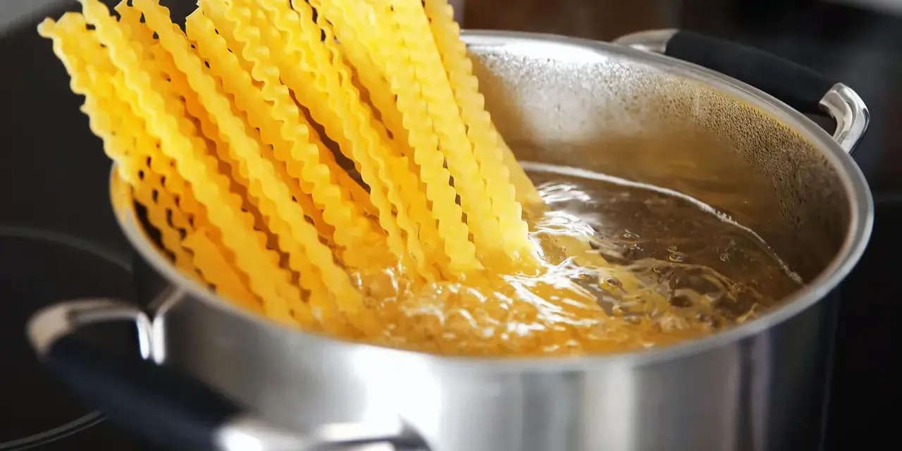 Lange, gewellte vermicelli noodles kochen in sprudelndem Wasser in einem Edelstahltopf.
