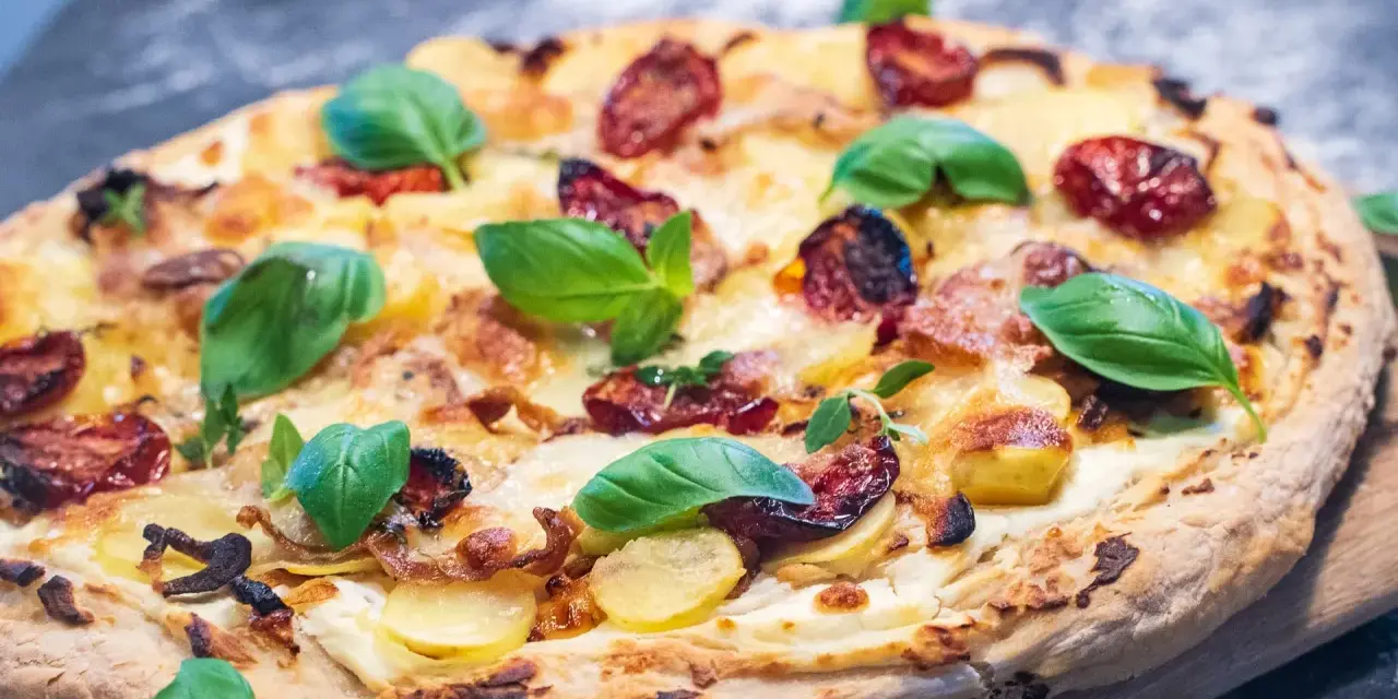 Leckeres Pizza Bianca Rezept mit Kartoffelscheiben, getrockneten Tomaten und frischem Basilikum.