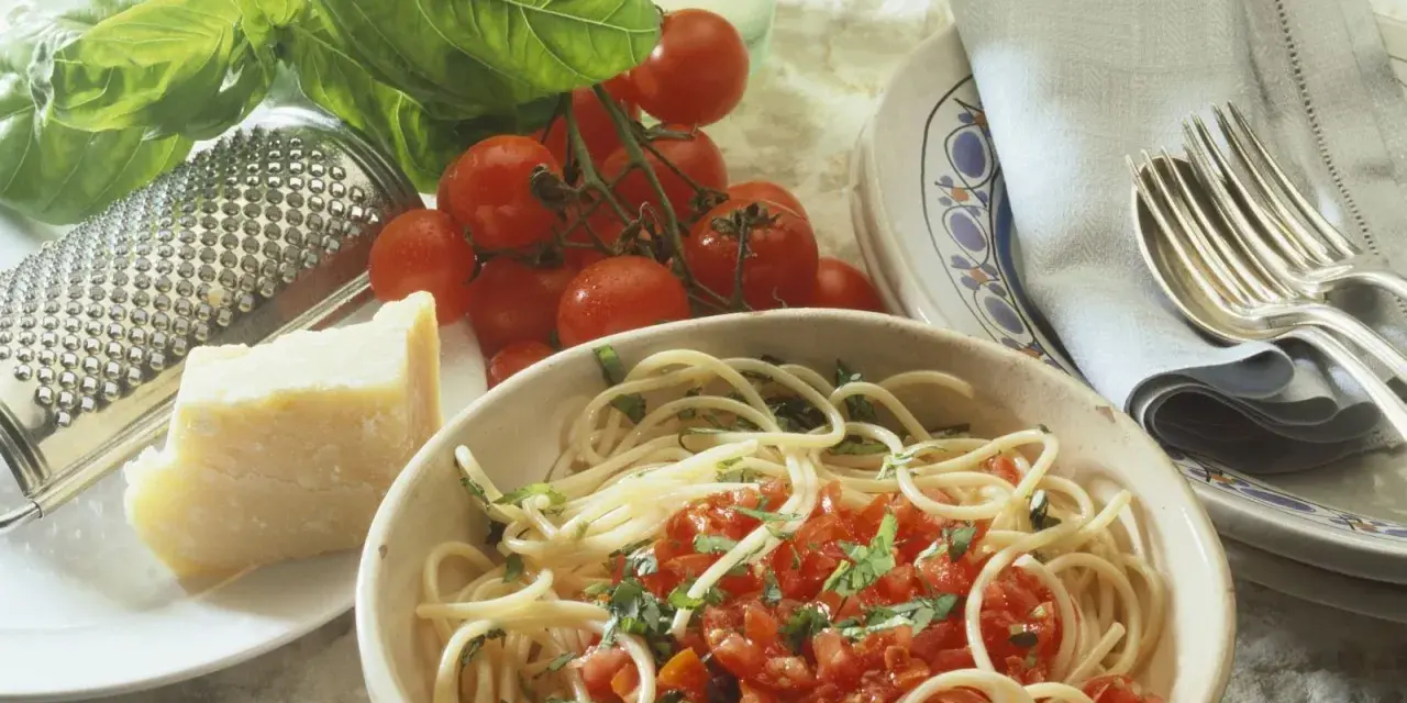 Spaghetti mit frischen Kräutern und gehackten Tomaten aus der Dose. Dazu ein Stück Parmesan, frische Tomaten und ein Grater. Perfekt für einfache Rezepte mit gehackten Tomaten aus der Dose.