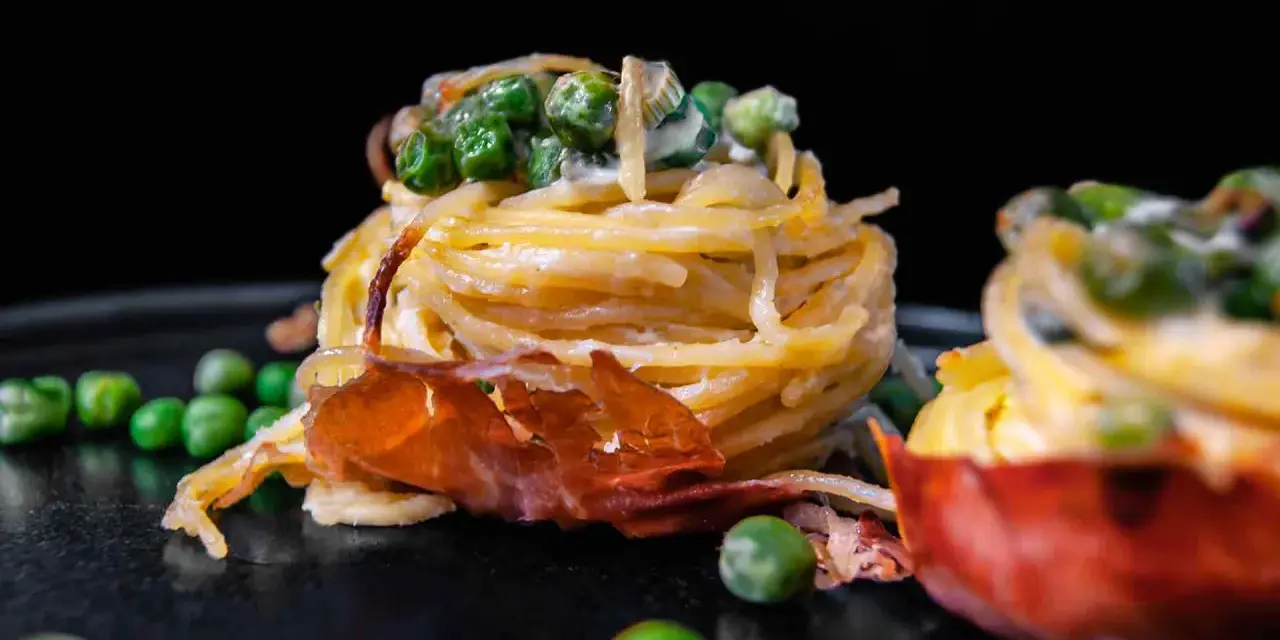 Köstliche italienische Pasta Vorspeisen mit Erbsen und Schinken, auf einem dunklen Teller angerichtet.