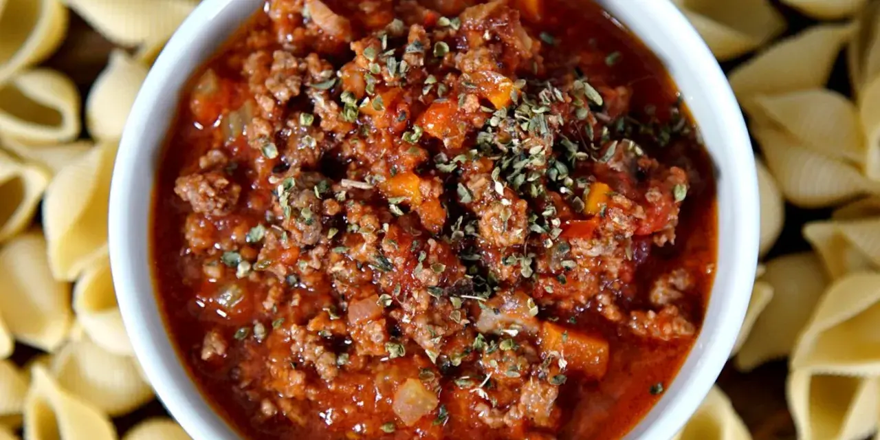 Herzhafte pancetta bolognese in einer Schüssel, umgeben von ungekochten Muschelnudeln.