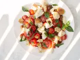 Ein frischer Tomaten Mozzarella Salat, original italienisch, mit Brotstücken und Basilikum, serviert auf einem weißen Teller.