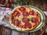 Eine köstliche Pizza Salami mit geschmolzenem Käse und frischem Basilikum auf einem rustikalen Holztisch.