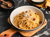 Eine Schüssel cremiger Pasta Carbonara, garniert mit frisch geriebenem Parmesan und schwarzem Pfeffer, bereit zum Genießen.