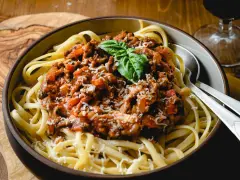 Herzhafte bolognese mit speck, serviert auf Bandnudeln, garniert mit Basilikum und Parmesan.