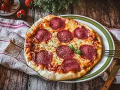Eine köstliche Pizza Salami mit geschmolzenem Käse und frischem Basilikum auf einem rustikalen Holztisch.
