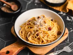 Eine Schüssel cremiger Pasta Carbonara, garniert mit frisch geriebenem Parmesan und schwarzem Pfeffer, bereit zum Genießen.