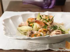 Frischer insalata di mare mit Garnelen, Muscheln und Tintenfischringen, garniert mit Kräutern und Zwiebelringen.