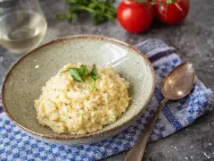 Cremiges Risotto, perfekt als Grundrezept für viele Variationen. Mit frischer Petersilie garniert, daneben ein Glas Weißwein und Tomaten.