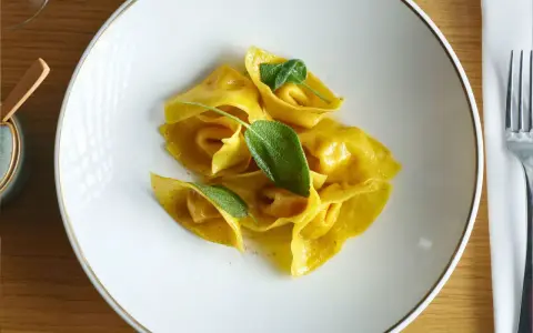 Gelbe Ravioli mit Salbeiblättern auf einem weißen Teller. Ein köstliches Gericht, das zeigt, was ist Ravioli: gefüllte Teigtaschen.