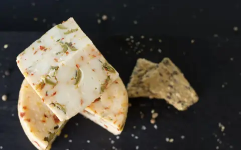 Käse mit Kräutern und Paprika, eine köstliche pecorino alternative, neben knusprigen Crackern auf dunklem Untergrund.