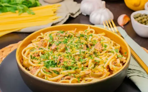 Eine Schüssel mit Thunfisch Pasta, garniert mit Petersilie und Zitronenschale. Oliven und Kapern sind ebenfalls sichtbar.