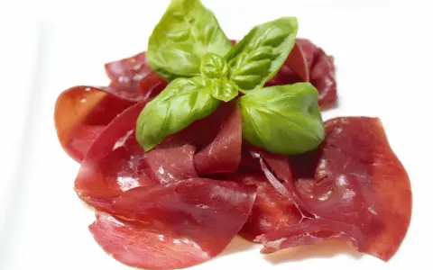 Dünne Scheiben von Bresaola, einem luftgetrockneten Rindfleisch, garniert mit frischem Basilikum.