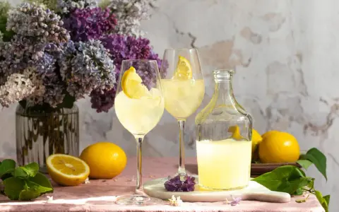 Erfrischender Limoncello Spritz mit Bitter Lemon, garniert mit Zitronenspalten, neben frischen Zitronen und einem üppigen Fliederstrauß.