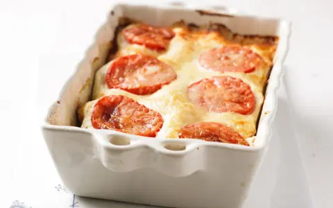 Gorgonzola Lasagne mit Tomaten und geschmolzenem Käse in einer weißen Auflaufform.