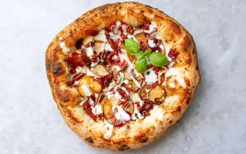 Eine köstliche Pizza aus Neapel mit Kartoffelscheiben, Speck, Nüssen und einem Hauch von Basilikum.