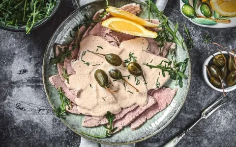Vitello Tonnato Rezept Original Italienisch: Dünne Kalbfleischscheiben mit cremiger Thunfischsauce, Kapern und Zitronenspalten auf einem Teller.