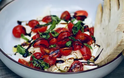 Burrata Caprese Salat mit Kirschtomaten, Basilikum und Balsamico-Dressing, serviert in einer Schüssel mit Holzsalatbesteck.