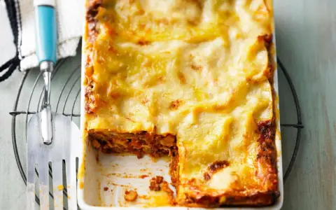 Eine goldbraun überbackene Lasagne mit einer cremigen Käseschicht. Ein Stück ist bereits entnommen, was die saftige Füllung offenbart. Diese Pistazien Lasagne sieht köstlich aus!