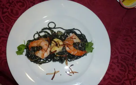 Schwarze Spaghetti mit Garnelen, garniert mit Koriander und knusprigen Zwiebeln. Ein köstliches Gericht, das auf einem weißen Teller serviert wird.