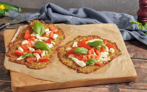 Zwei leckere Zucchini-Pizzen mit Mozzarella, Tomaten und Basilikum auf Backpapier.