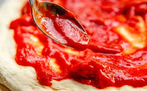 Eine Löffelspitze verteilt die original italienische pizzasauce auf einem Pizzateig.