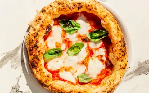 Eine echte italienische Pizza Margherita mit geschmolzenem Mozzarella, Tomatensauce und frischem Basilikum auf einem Marmortisch.