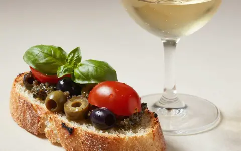 Bruschetta mit Olivencreme, Tomaten und Basilikum. Ein Glas Weißwein daneben. Perfekt für ein schnelles olivencreme rezept.