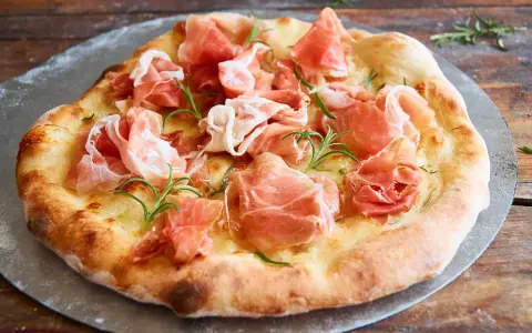 Eine köstliche biancaneve pizza mit zartem Schinken und Rosmarin, auf einem Pizzastein serviert.