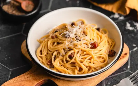 Eine Schüssel cremiger Pasta Carbonara, garniert mit frisch geriebenem Parmesan und schwarzem Pfeffer, bereit zum Genießen.
